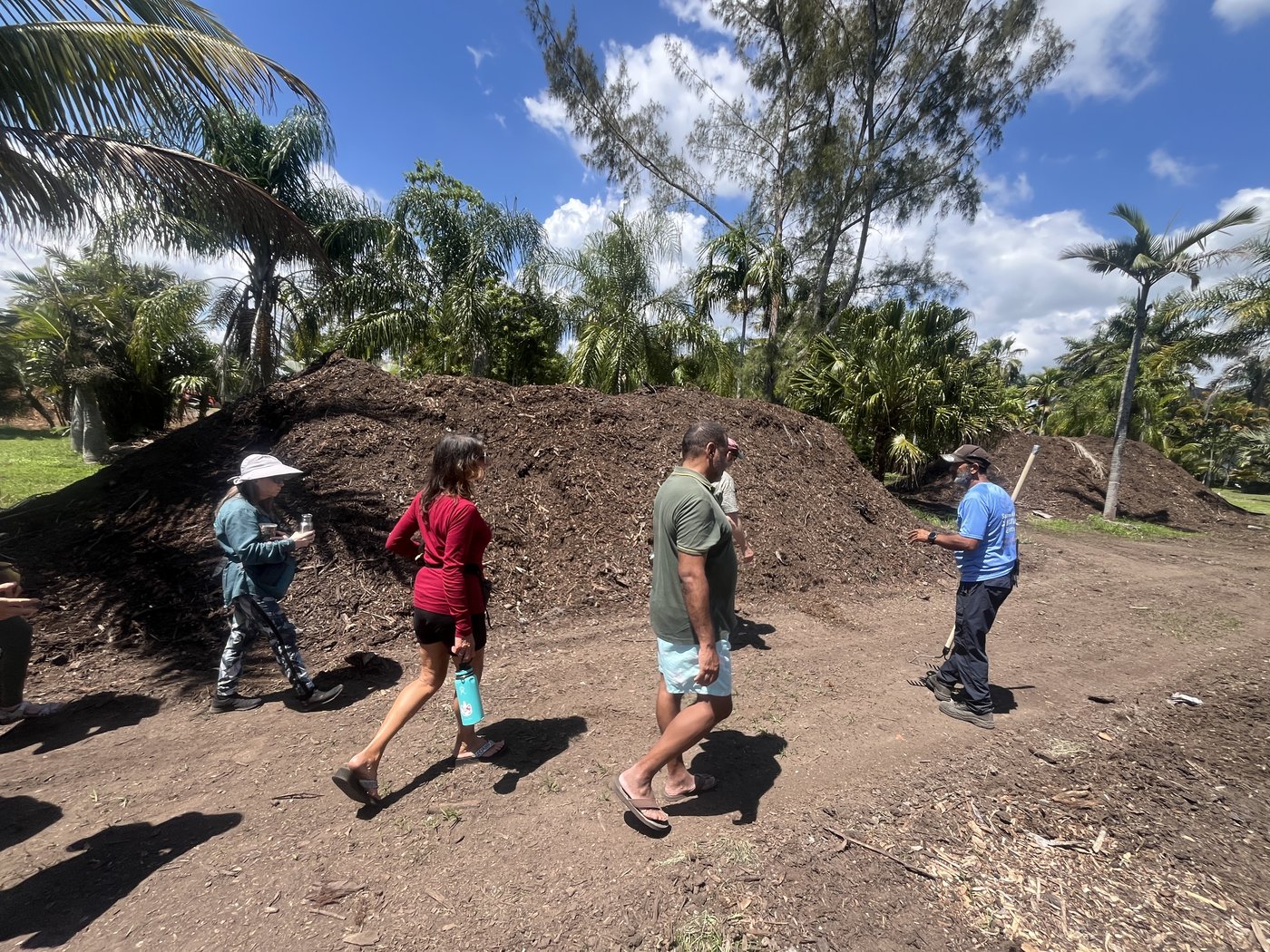 Workshop group walking a farm path beside mulch and compost windrows